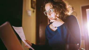 mujer mirando un papel mientras usa su computadora analizando el cuit
