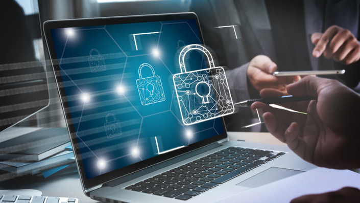 Una computadora mostrando una alerta de seguridad, con un gráfico de transacciones en segundo plano.