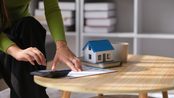 Una persona con una calculadora y algunos papeles y una casita simulando el tipo de interés de préstamos personales.