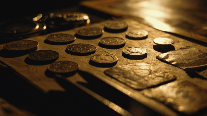 Colección de monedas antiguas dispuestas sobre una superficie de madera rústica con iluminación cálida y dorada