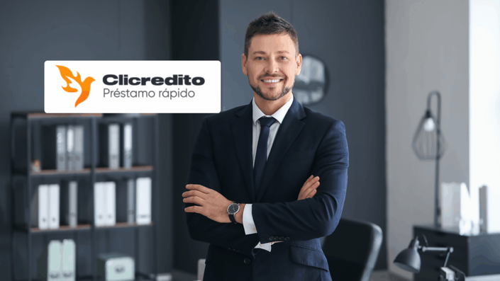 Hombre de negocios sonriente con traje azul y brazos cruzados, en oficina elegante con logo de Clicredito Préstamo rápido superpuesto.