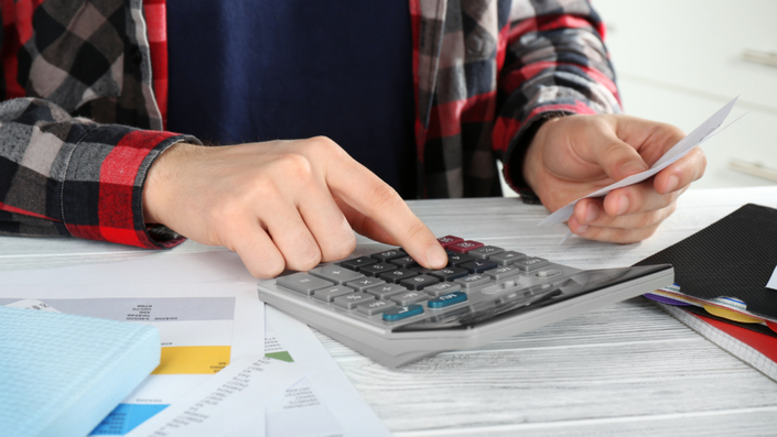 Persona sentada moviendo papeles y sumando en una calculadora