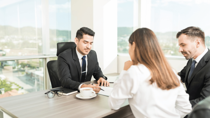 Asesor financiero explicando condiciones de microcréditos a una pareja emprendedora en una reunión profesional, destacando la importancia del financiamiento para negocios.