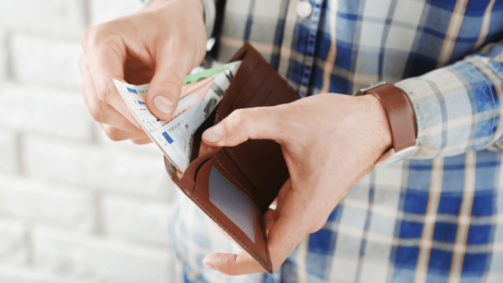 Hombre sacando billetes de su billetera. Administrar bien el dinero es clave para reducir gastos y evitar problemas financieros.