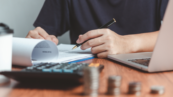 Hombre tomando notas en su cuaderno junto a una calculadora y monedas.