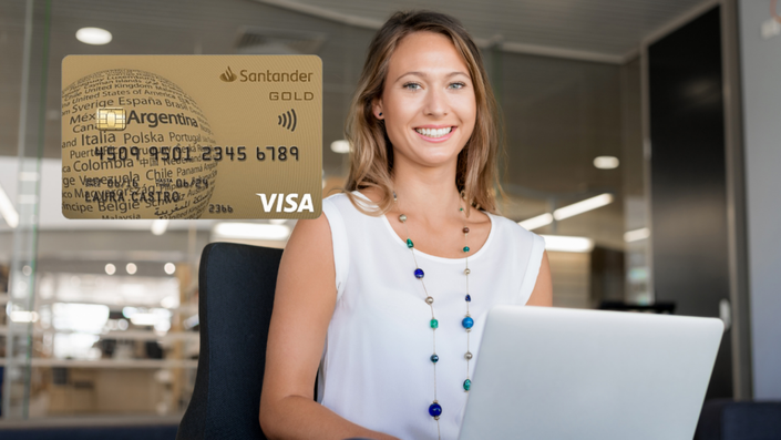 Mujer sonriente con una tarjeta Santander Gold Visa en primer plano, trabajando en su computadora portátil en una oficina moderna. Imagen relacionada con tarjetas de crédito Santander.
