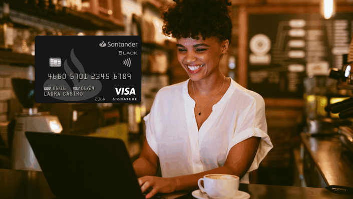 Mujer sonriente trabajando en laptop en una cafetería con tarjeta Santander Black Visa Signature superpuesta.