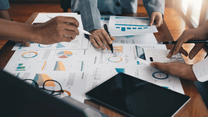 Varias personas analizando gráficos y reportes financieros sobre una mesa, utilizando calculadora y bolígrafos, en una reunión de trabajo enfocada en la evaluación de bonos argentinos.