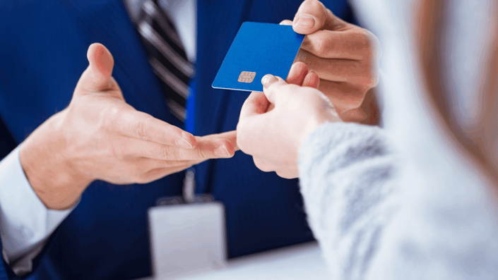 Una persona entregando una tarjeta de crédito azul en una oficina bancaria durante el proceso de cómo cancelar tu tarjeta de crédito, mostrando la entrega física del plástico al ejecutivo.