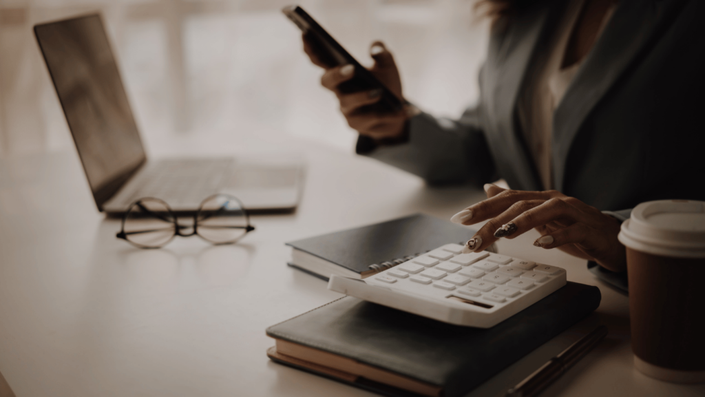 Persona utilizando una calculadora y teléfono móvil mientras organiza sus finanzas, representando cómo salir del endeudamiento mediante el uso de herramientas para gestionar deudas.