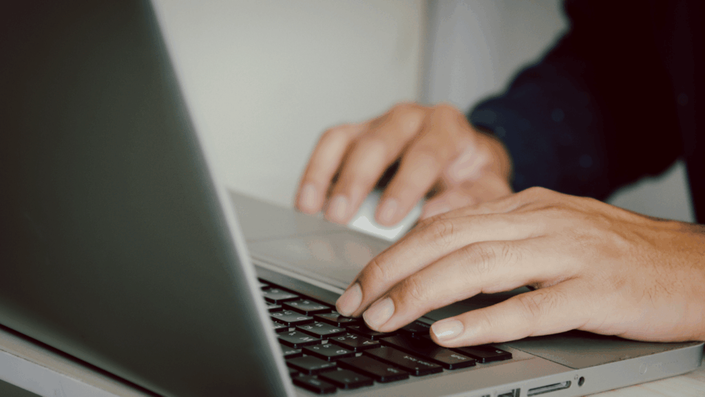Manos de una persona usando una computadora portátil, con el dedo índice en el teclado y la otra mano en el mouse, representando la búsqueda en línea sobre dónde vender monedas antiguas en México al mejor precio.