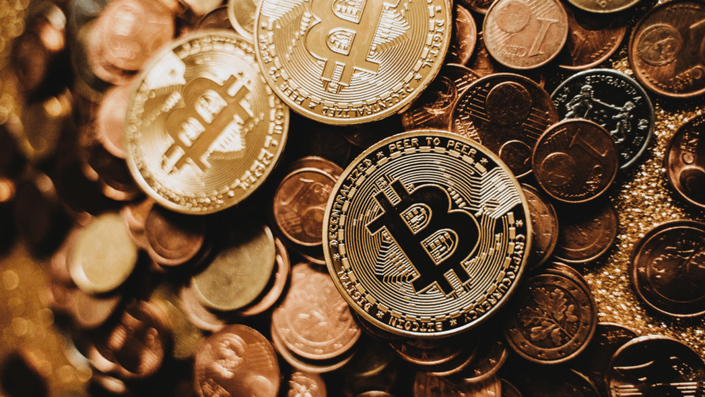 Varias monedas físicas de Bitcoin mezcladas con monedas tradicionales de euro, simbolizando la convivencia de las Criptomonedas con el dinero fiat en Argentina.