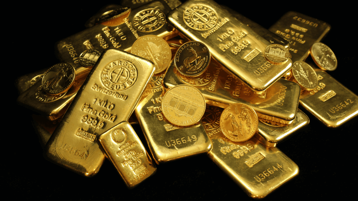 Colección de monedas de oro de diversos países junto a pequeños lingotes, representando diferentes formas físicas de invertir en oro.