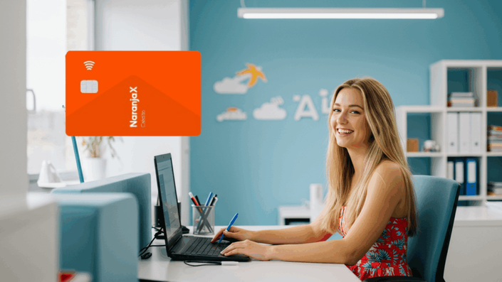 Joven feliz en un entorno de oficina colorido, usando una laptop, con una tarjeta de crédito Naranja X destacada en la imagen.