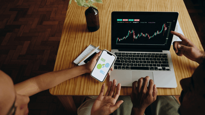 Dos personas concentradas analizando gráficos de la fluctuación del precio del oro en una pantalla de computadora, estrategia clave al invertir en oro.
