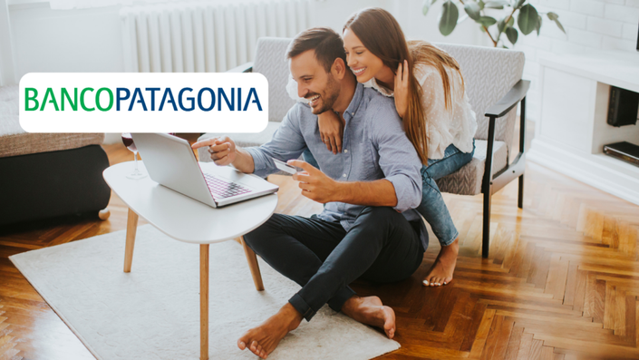 Pareja sonriendo mientras miran una computadora portátil en su sala de estar, con el logo de Banco Patagonia sobreimpreso en la esquina superior izquierda.