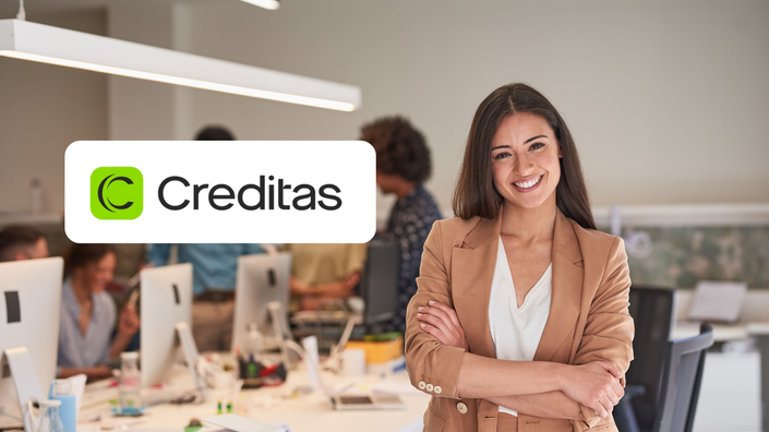 Profesional sonriendo en una oficina moderna con el logo de Creditas destacado.