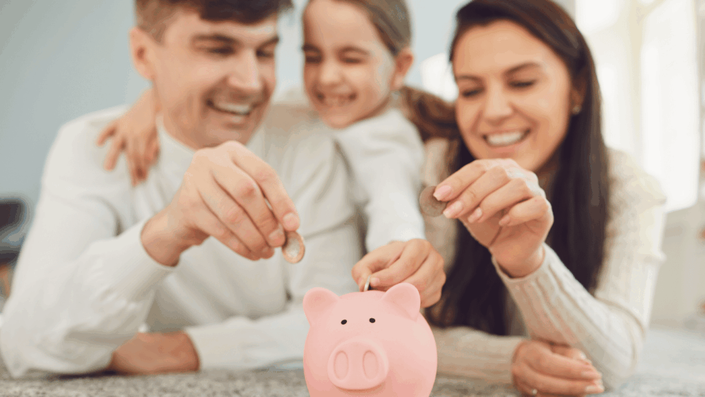 Familia feliz, incluyendo una niña, administrando su presupuesto familiar en México mientras colocan monedas en una alcancía juntos.