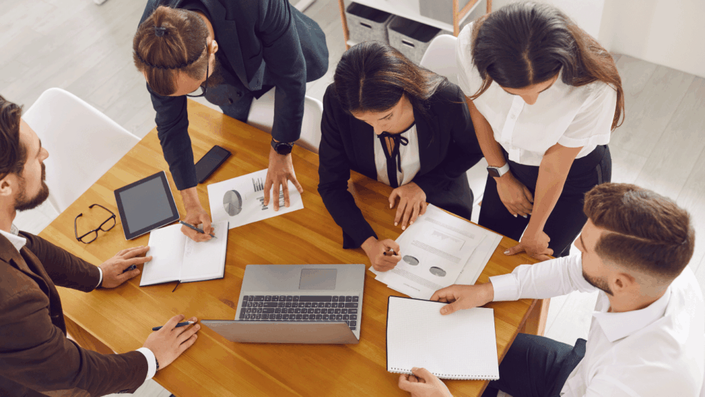 Un equipo de profesionales colaborando en una mesa, discutiendo estrategias financieras sobre las tandas en México mientras revisan gráficos y notas.